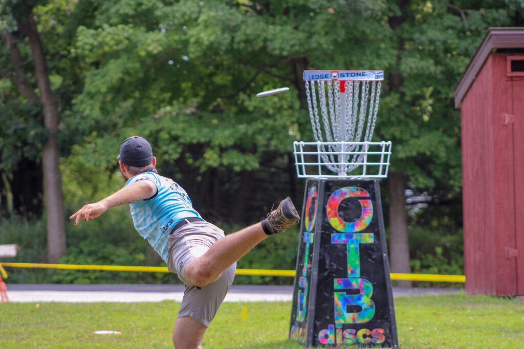 A man throws a disc toward a basket while playing disc golf.