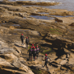 A group goes coasteering along a rocky beach.