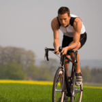 A man cycling past green fields.