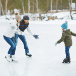 An ice skating mom and dad encourage their child to skate toward them.