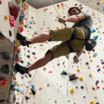 A man uses ropes to climb a tall indoor wall.