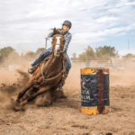 A woman riding a horse around a barrel.