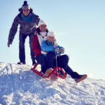 A man helping his wife and child start sledding downhill.