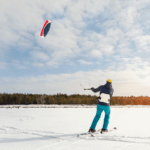 A man snow kiting across an open snowy field.