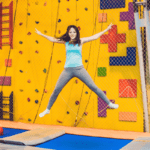 A woman jumps on a blue trampoline inside a gym.