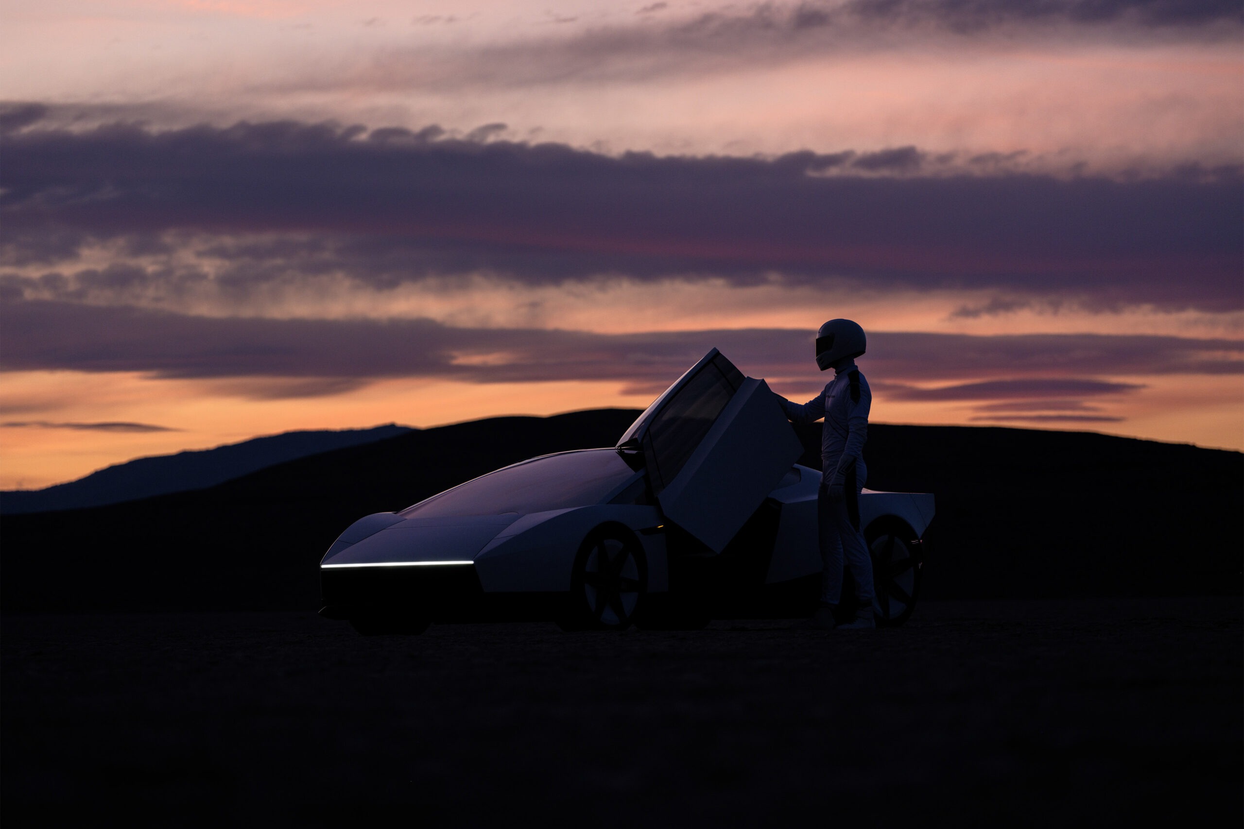 A driver in a racing suit stands by the open door of the Roadster at dusk