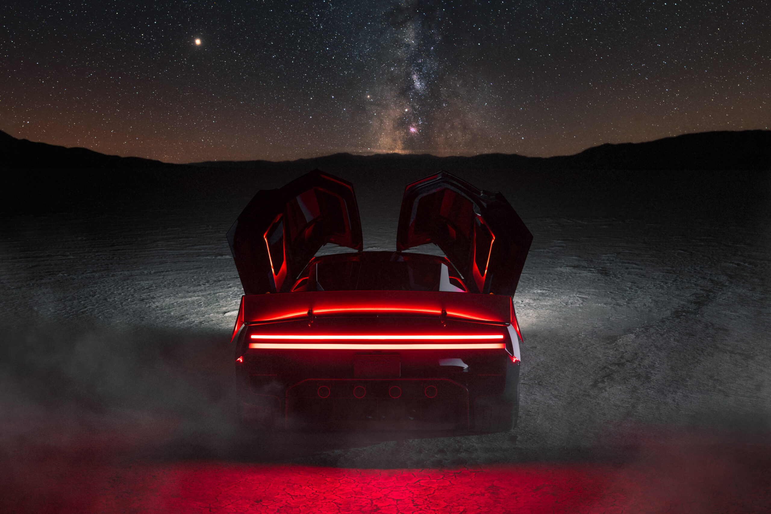 The Roadster under a starry sky with doors open and its red rear light bar glowing