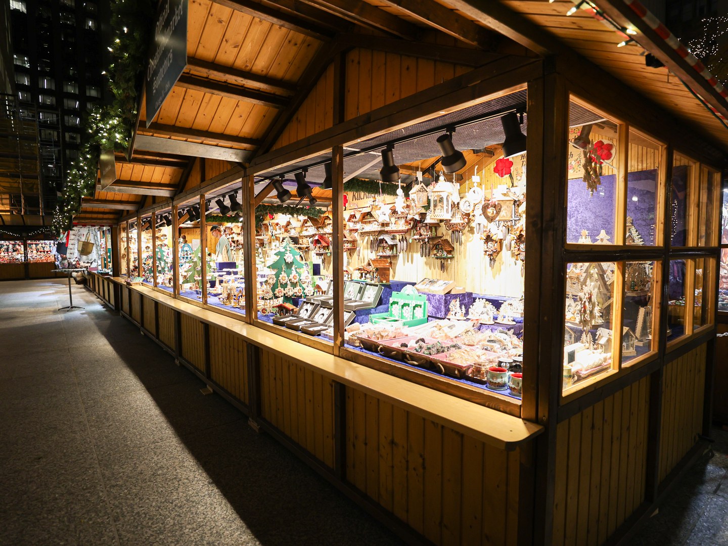 A long wooden market stall lit from inside, its windows filled with cuckoo clocks, carved wooden ornaments and small Christmas decorations