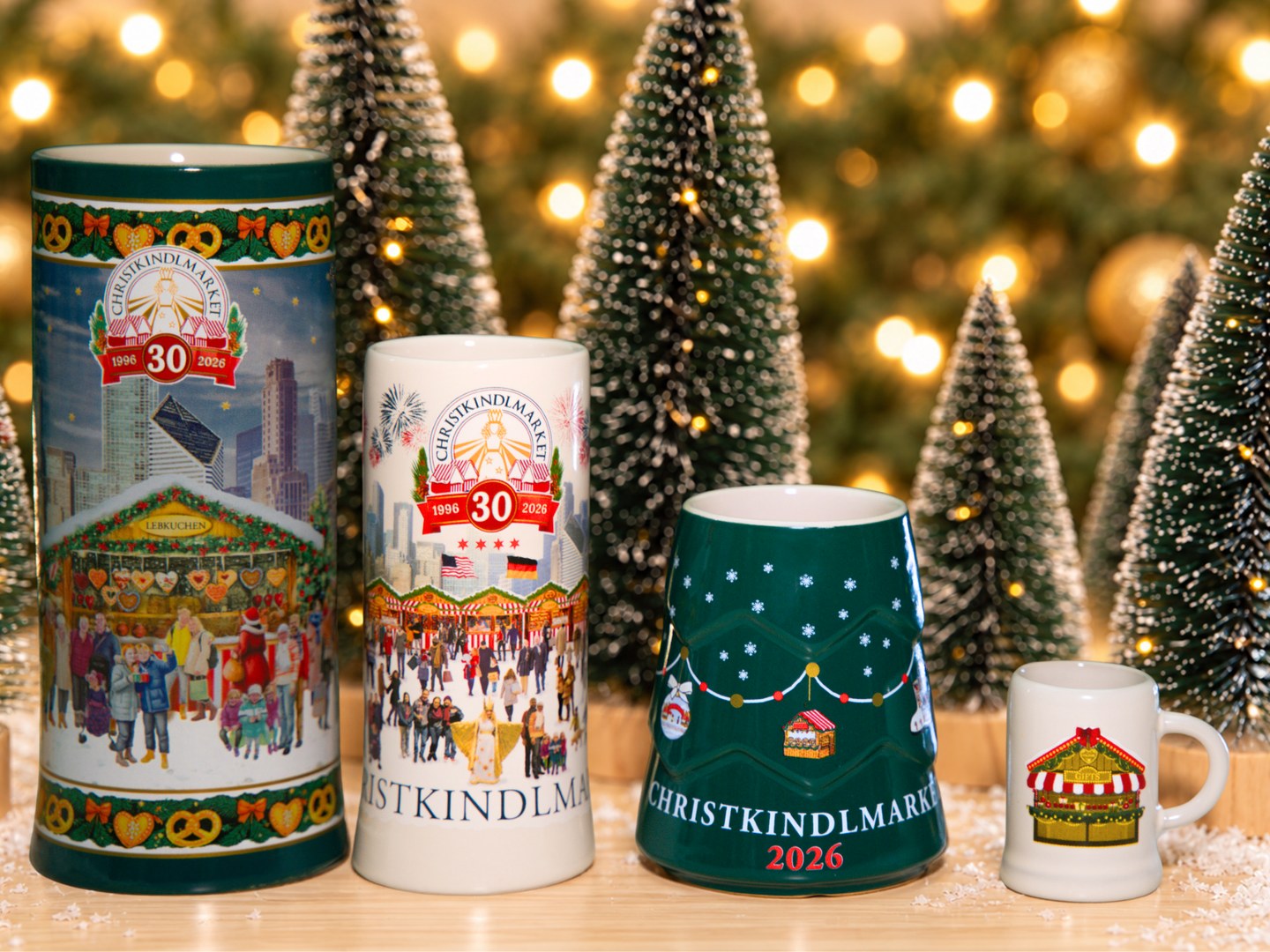 Four ceramic Christkindlmarket souvenir mugs, two tall steins with 30th anniversary artwork, a green tree shaped mug and a tiny stein, set among miniature Christmas trees