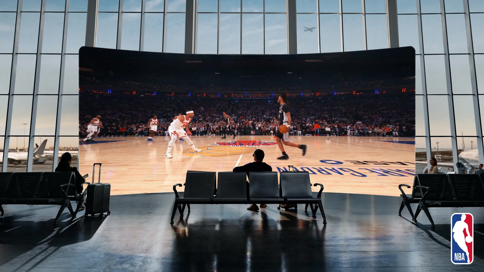 Person watching a giant virtual NBA game screen while seated in an airport lounge