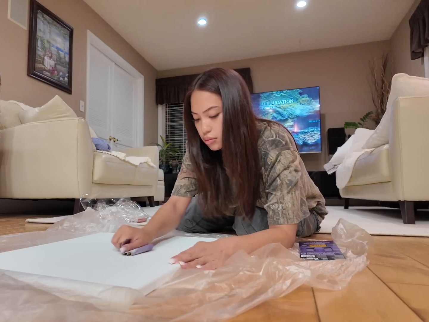 Woman kneeling on a living room floor preparing a blank canvas for a painting session