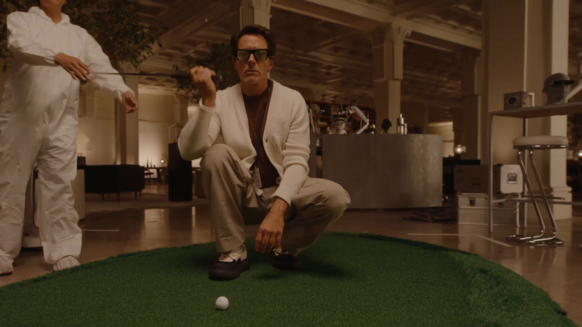 Robert Downey Jr. crouches on an indoor putting green wearing Snap Specs glasses, studying the line of his putt