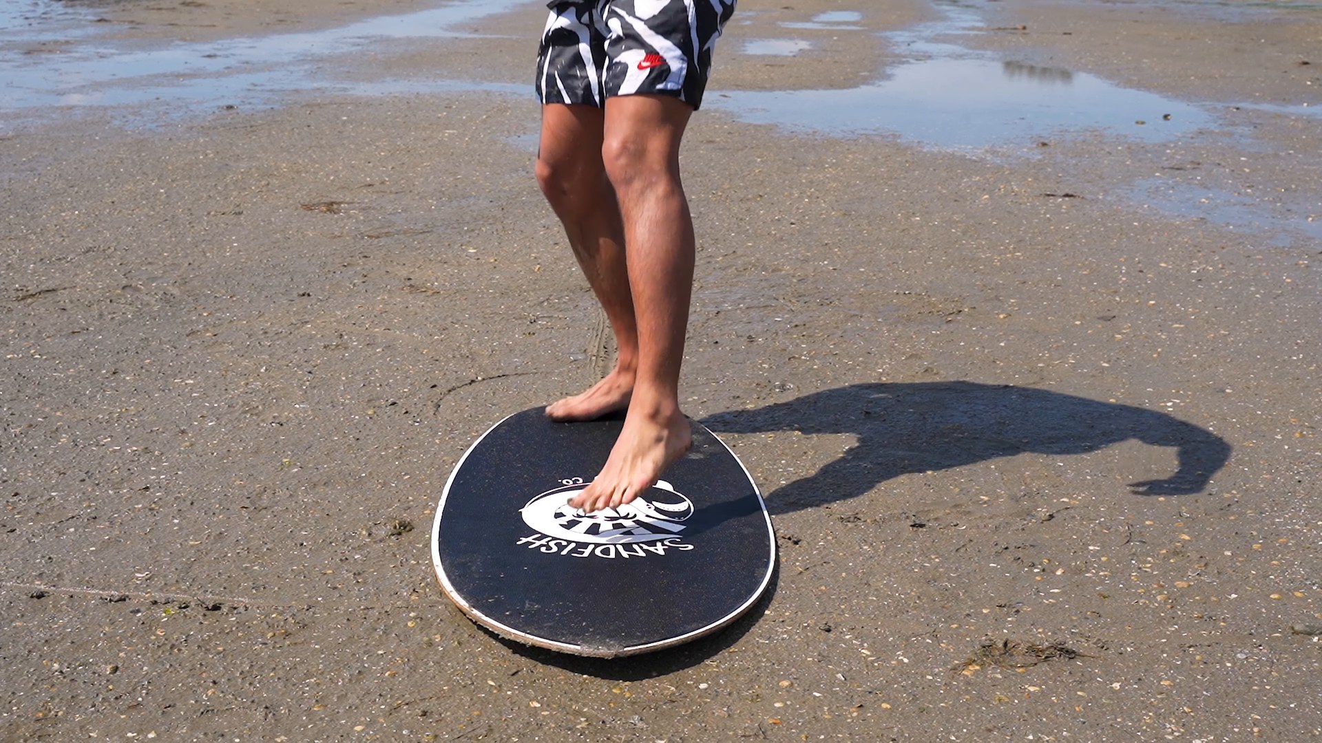 A skimboarder stepping onto his board on wet sand